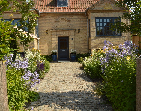 Farver i hus bygget i engelsk stil var inspiration for staudebede i gult, hvidt og blåviolet på hver side af indgangssti i chaussésten. Havearkitekt gruppen